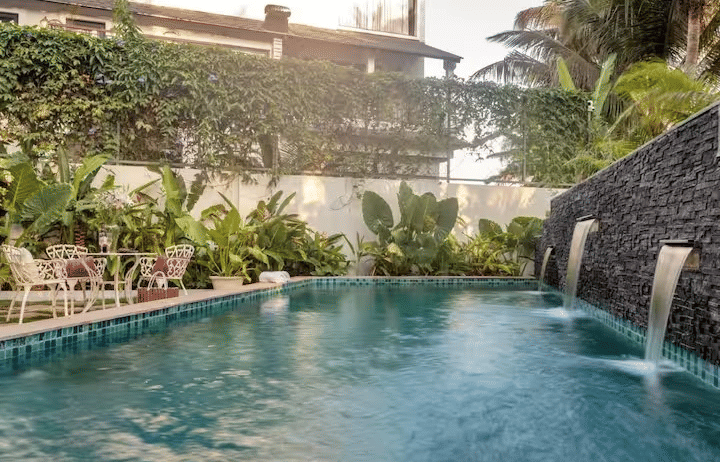 Swimming pool with a waterfall feature and lush plants surrounding the area at Lime Tree Villa with Private Pool | Luxury Stay in Goa.